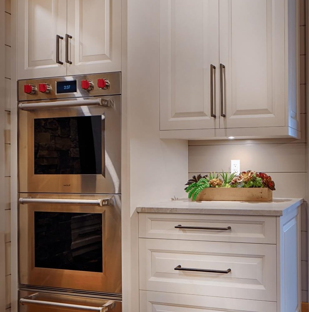 Project_Kitchens_Fruit+Ridge11 Modern kitchen cabinetry with double ovens, sleek white finish, and a countertop displaying a small arrangement of succulents.