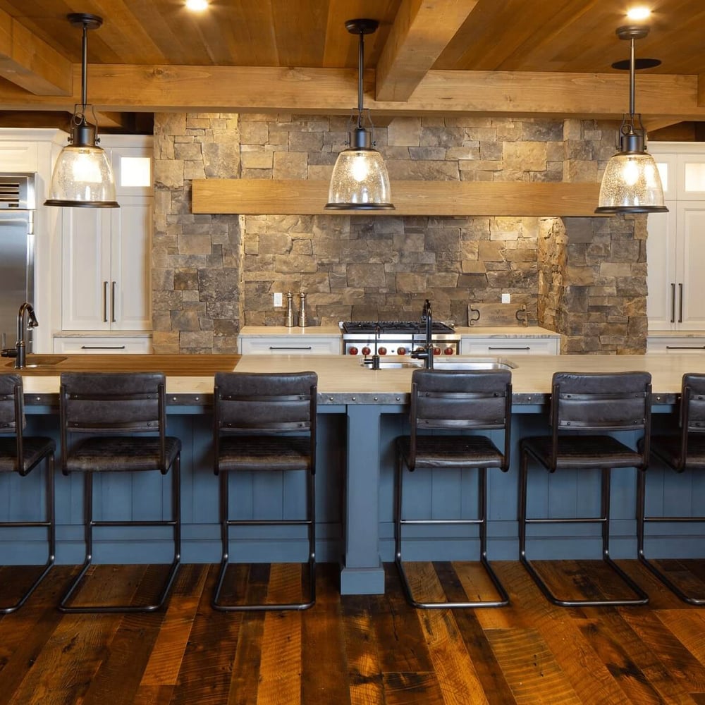 Project_Kitchens_Fruit+Ridge3 Modern kitchen with a stone accent wall, featuring a large island with six dark bar stools and pendant lighting above.
