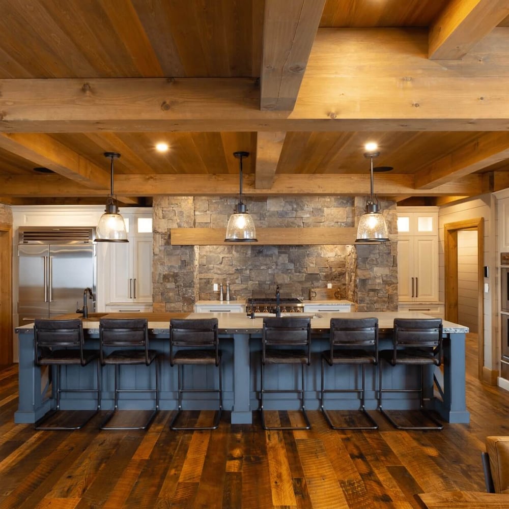 Project_Kitchens_Fruit+Ridge4 Modern kitchen featuring a large island with bar stools, wooden beams, stone accents, and stainless steel appliances.