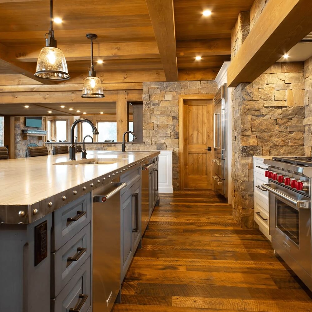 Project_Kitchens_Fruit+Ridge5 Modern kitchen with a large island, stainless steel appliances, stone accents, and wooden beams in a rustic design.