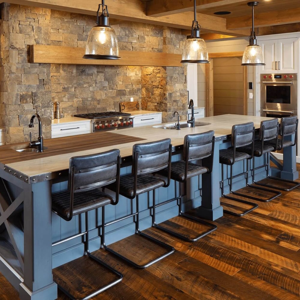 Project_Kitchens_Fruit+Ridge_MAIN Modern kitchen with a large island featuring wooden countertops and bar stools, stone wall, and stainless steel appliances.