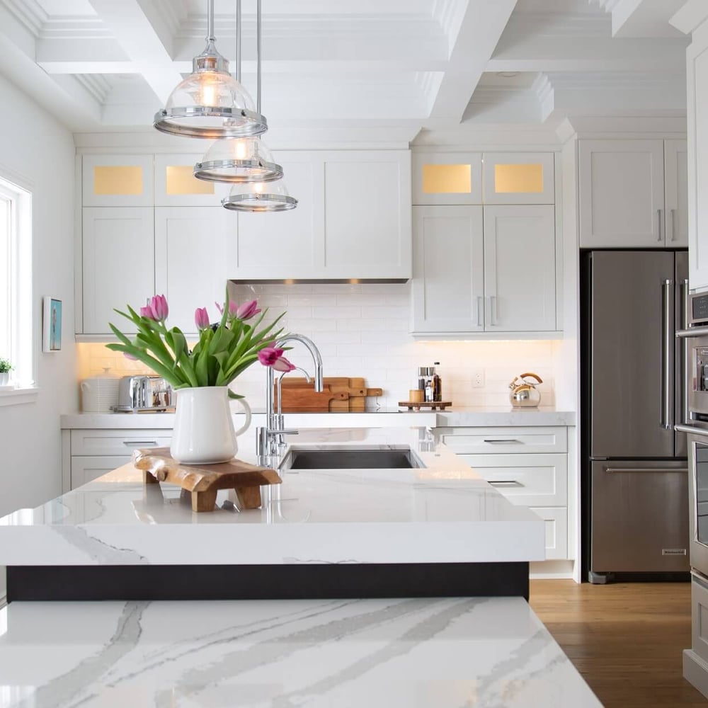 Modern kitchen with white cabinetry, stainless steel appliances, and a marble countertop adorned with a vase of tulips.