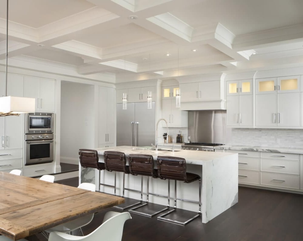 Project_Kitchens_Old+Colonial+Acres3 Modern kitchen with white cabinetry, marble island, stainless steel appliances, and wooden dining table with white chairs.