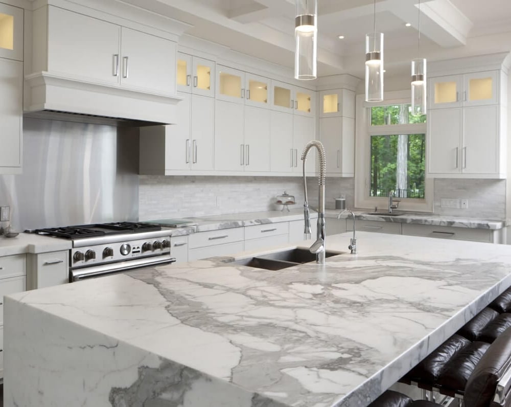 Project_Kitchens_Old+Colonial+Acres4 Modern kitchen with white cabinetry, a large marble island, and stainless steel appliances, featuring pendant lighting and a sleek design.