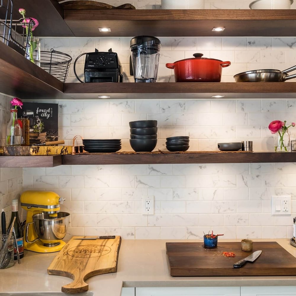 Project_Kitchens_Old+South9 Old South Kitchen by Casey's Kitchens features walnut floating shelves above a white marble subway tile backsplash, with a yellow mixer on the counter and black dishware stacked on shelves.