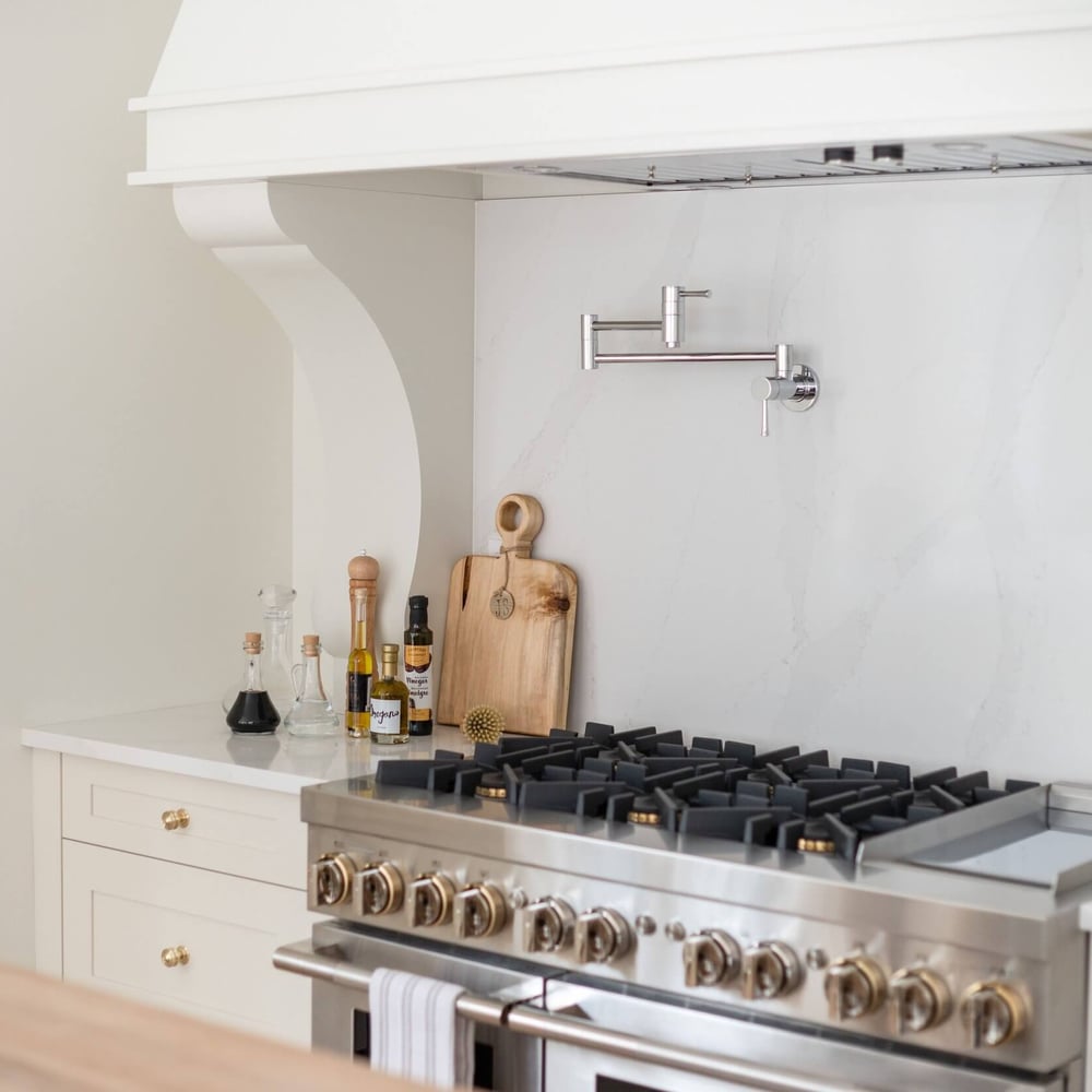 Stainless steel stove with a marble backsplash and wooden cutting board in a modern kitchen.