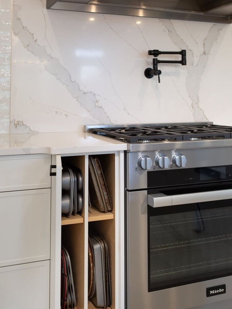A stainless steel Miele range sits below a marble-look backsplash with a pot filler and slim cabinet storage.