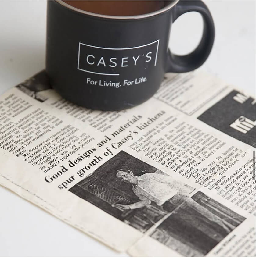 Black mug with 'CASEY'S' logo placed on a newspaper featuring an article about Casey's Kitchens and its designs.