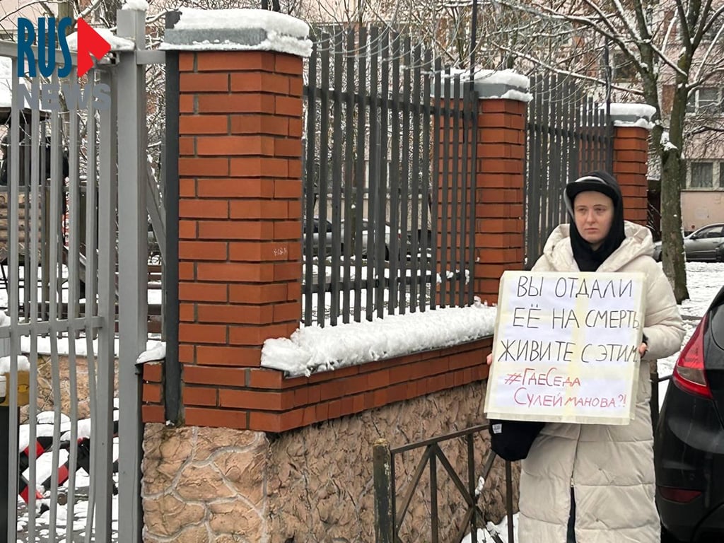 Lena Patyaeva stands outside a police station in St. Petersburg with a sign reading “You sent her to her death. Now live with it. Where is Seda Suleymanova?”, on 25 November 2025. Photo: RusNews
