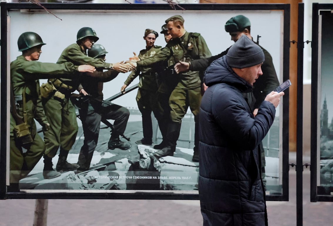 Прохожий с телефоном в руках у уличной фотовыставки, посвящённой окончанию Второй мировой войны, Санкт-Петербург, 27 ноября 2025 года. Фото: Анатолий Мальцев / EPA