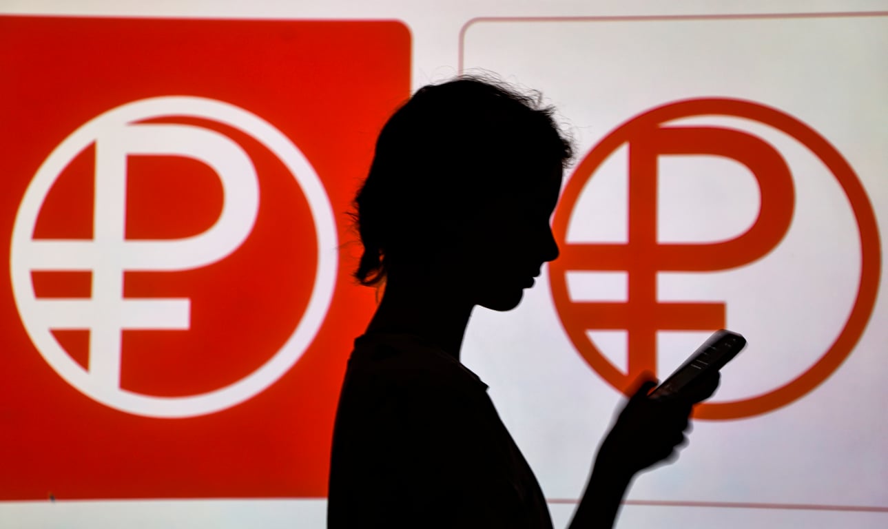 A woman stands in front of digital ruble logos in Moscow, 15 August 2023. Photo: EPA / SERGEI ILNITSKY