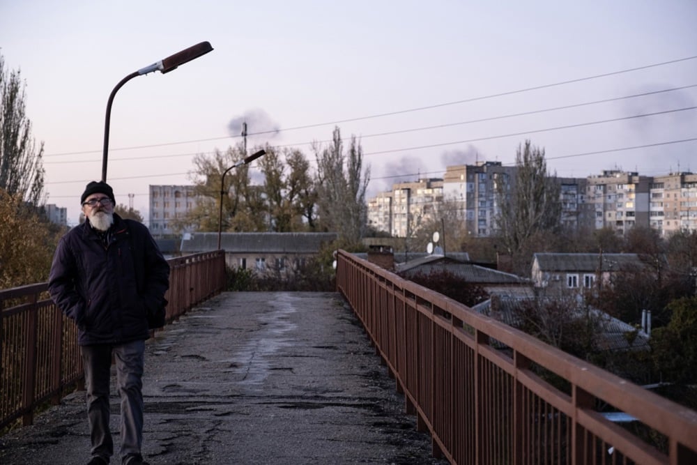 A Kherson resident walks across a bridge as smoke rises from Russian shelling, 16 November 2024. Photo: EPA/MARIA SENOVILLA