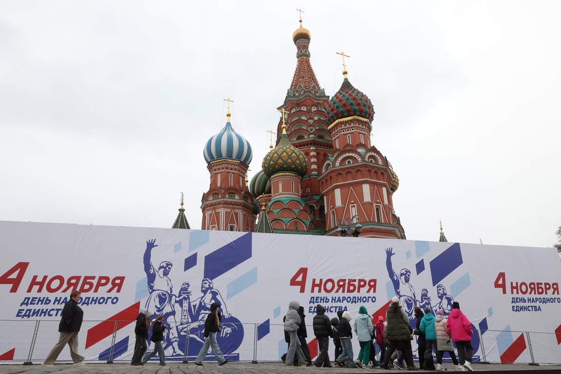 Люди проходят мимо постера с изображением памятника Минину и Пожарскому на Красной площади накануне Дня народного единства, Москва, 3 ноября 2025 года. Фото: Максим Шипенков / EPA