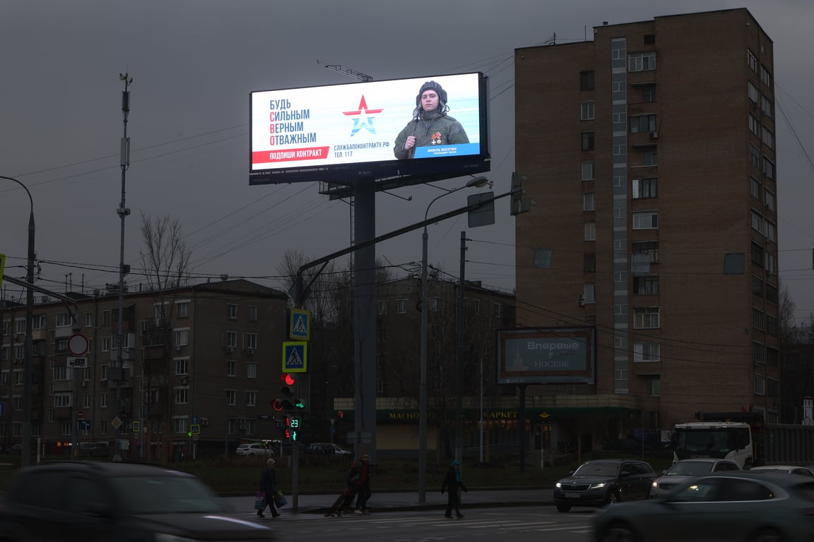 An poster encouraging people to enlist in the Russian military glows at dawn in a residential district of Moscow, 4 December 2025. Photo: EPA / Maxim Shipenkov