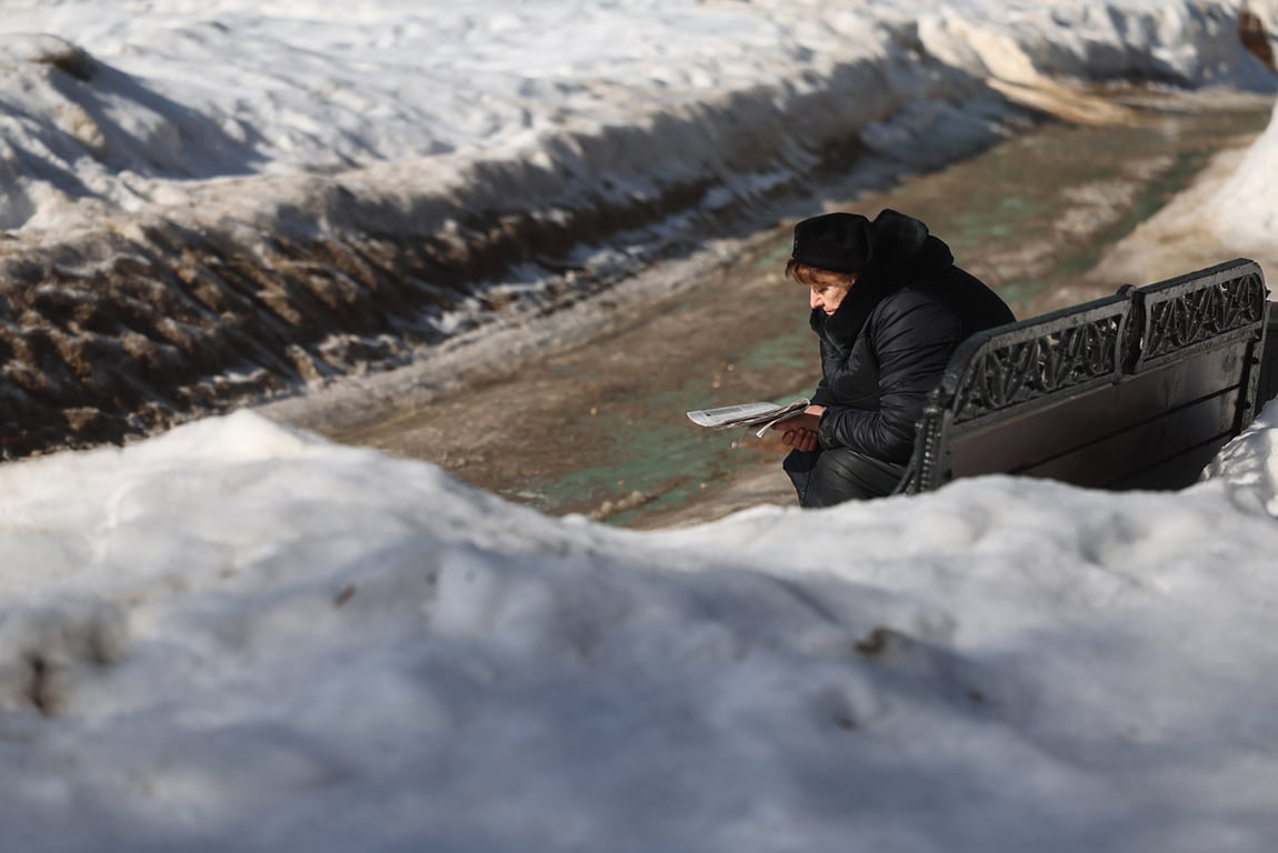 Женщина читает газету на скамейке в заснеженном парке Москвы, 10 марта 2026 года. Фото: Максим Шипенков / EPA