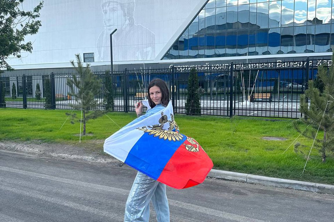 Maria Chushykina wrapped in a Russian flag near a sports centre in Mariupol, May 2024. Photo: Maria Chushykina / Telegram