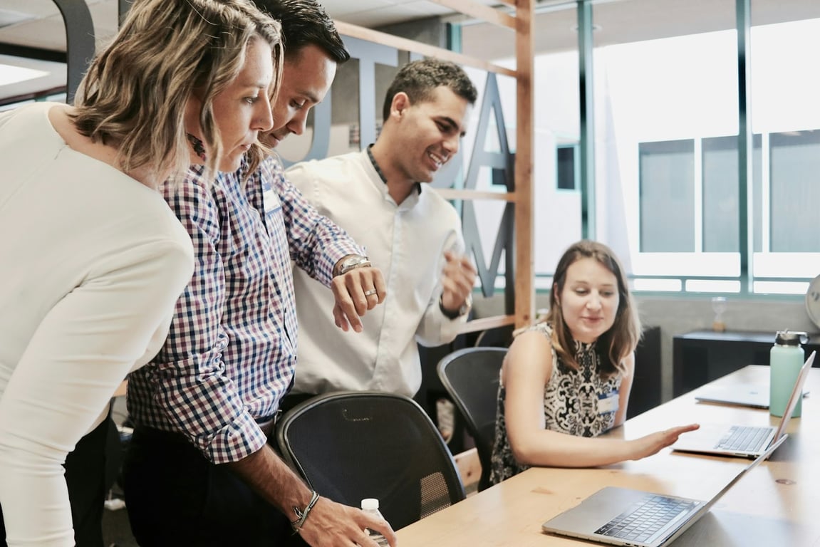 An office of young people standing around a laptop at a desk
