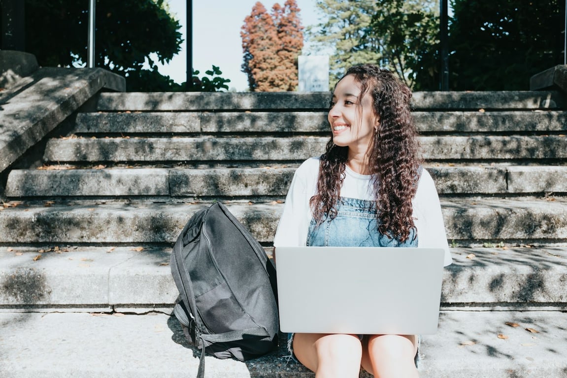 A Gen Z remote worker sits outside on some steps smiling