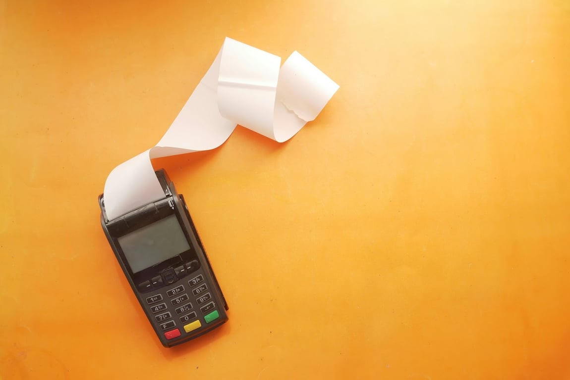 An old school card machine with a stream of paper on an orange background