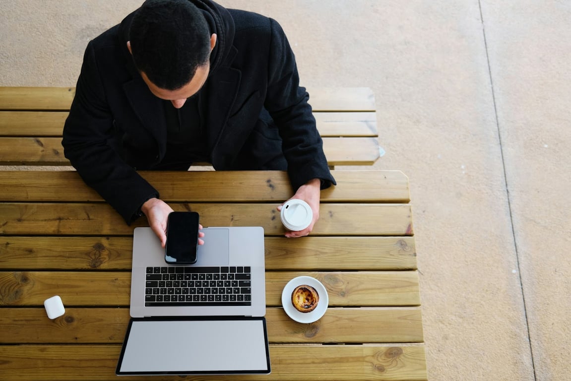 A tech job seeker sat at his laptop outside while on his smartphone