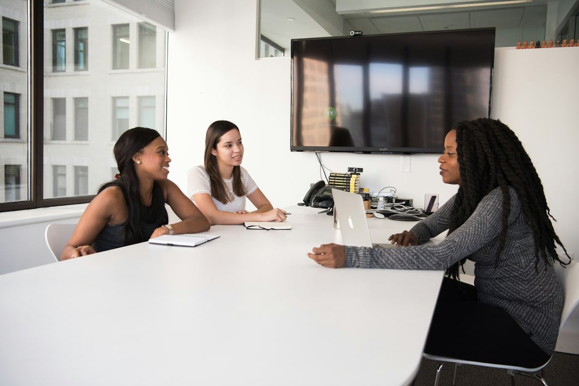 Three women in tech sit around an office table having a recruitment meeting