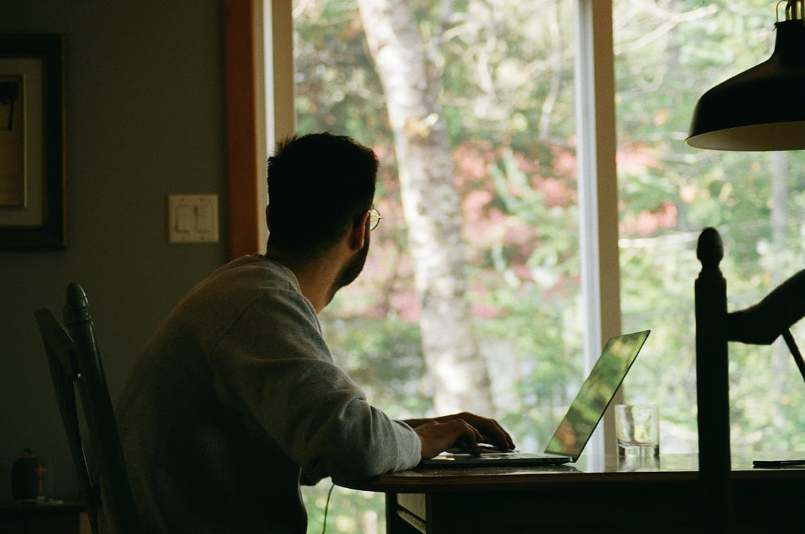 A remote worker looks out their window while working on their laptop at home