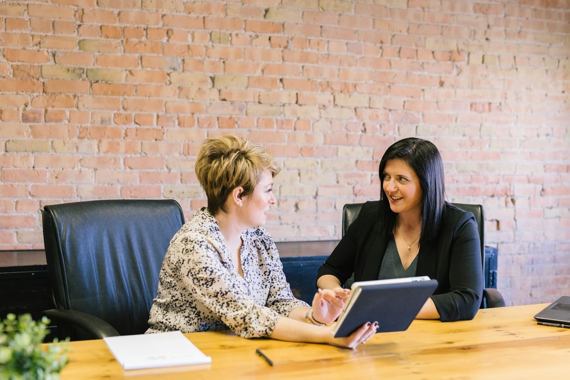 Two women discuss wage at a desk meeting with a tablet