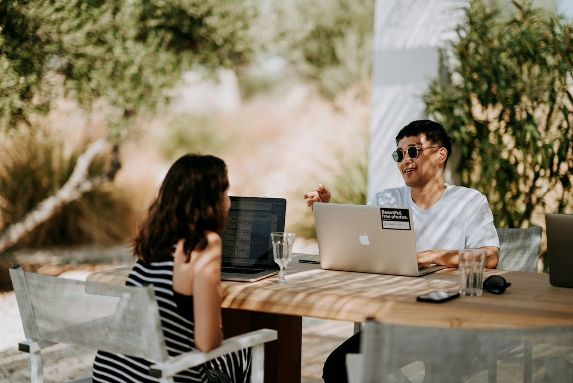 A guy and a girl on a workation on laptops out in the sun