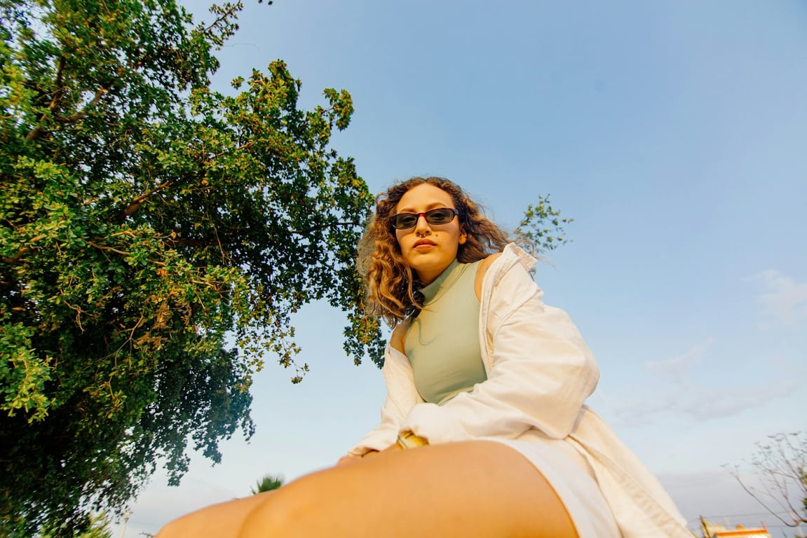 A Gen Z girl sits in a tree posing with sunglasses on