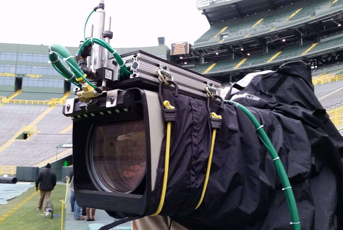 A camera with a Klear Shot non-contact lens cleaning system attached, in use during outdoor broadcast