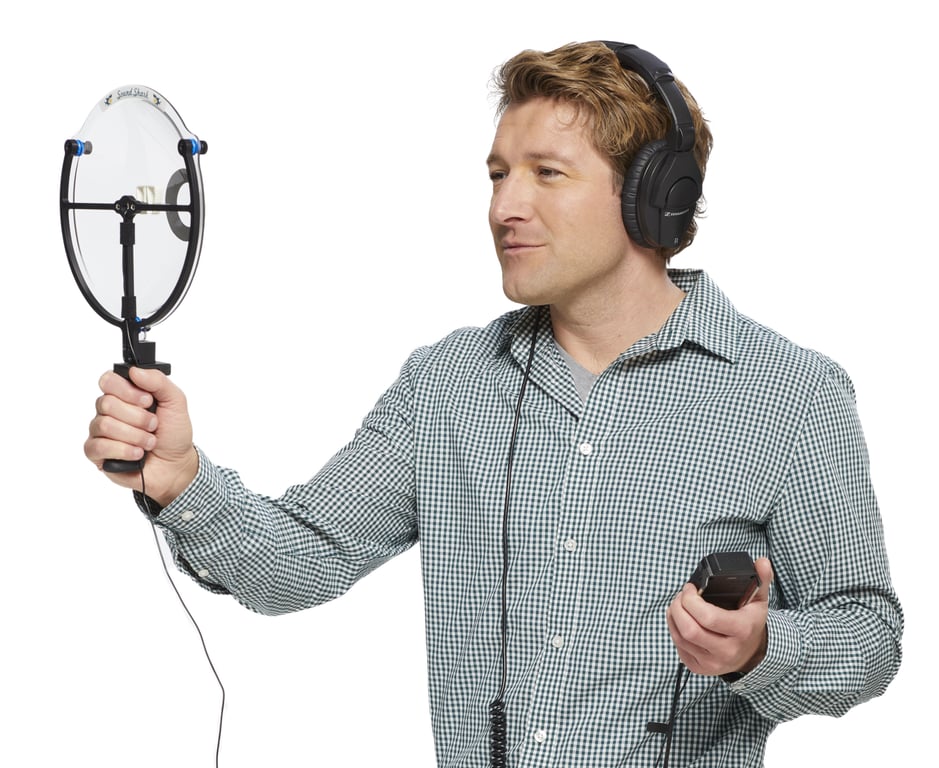 A man holding a Sound Shark long-range microphone while wearing headphones