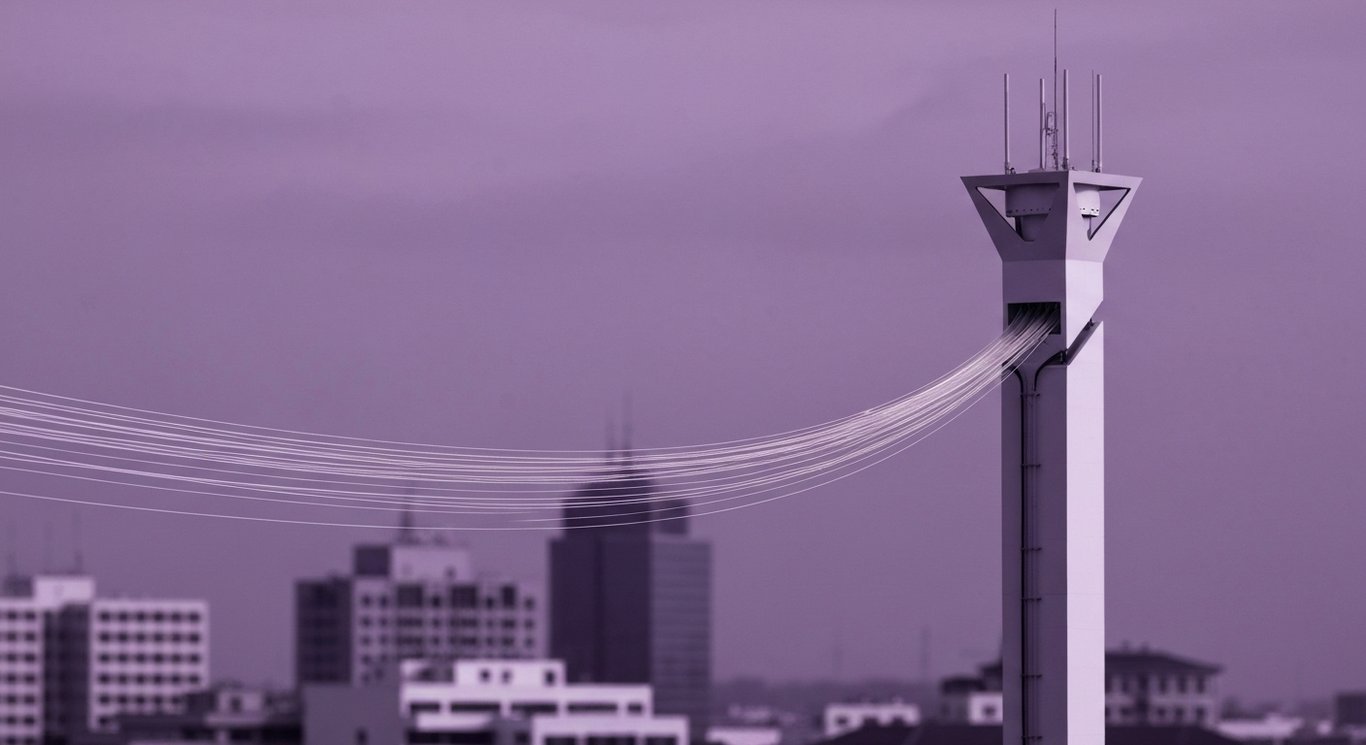 Fiber optic cables and a 5G tower stand before a softly lit city skyline with purple hues