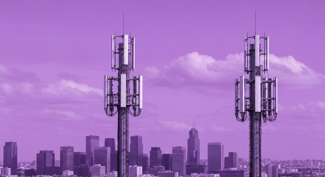 Two cell towers with antenna arrays in front of a city skyline and soft purple tones