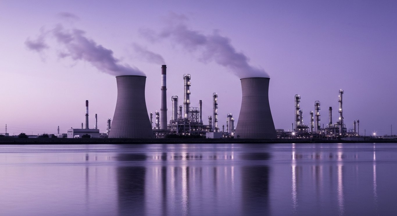Industrial refinery complex beside a river at dusk with purple-toned lighting