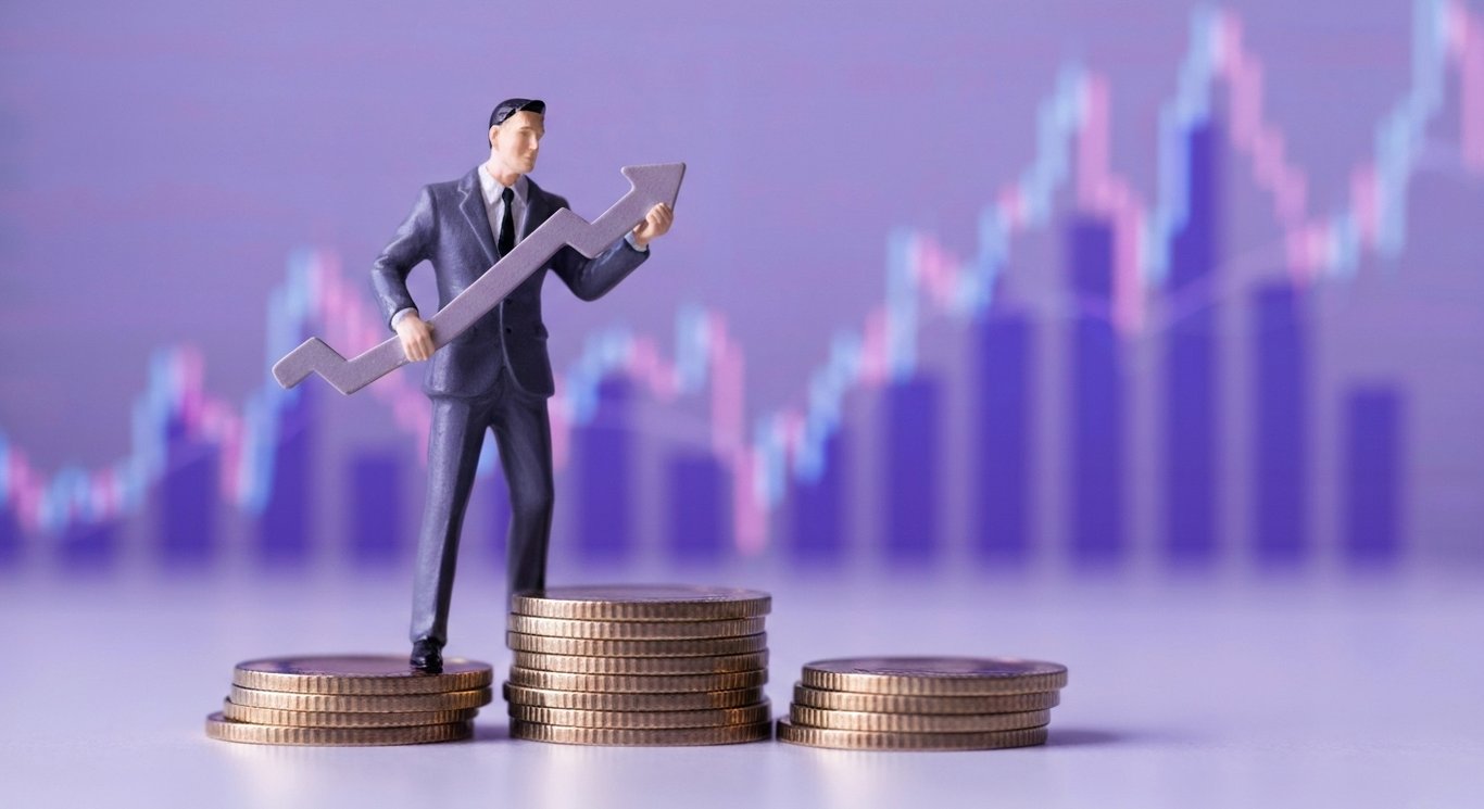 Businessman figurine with a red arrow pointing down, standing on coin stacks against a purple gradient graph background