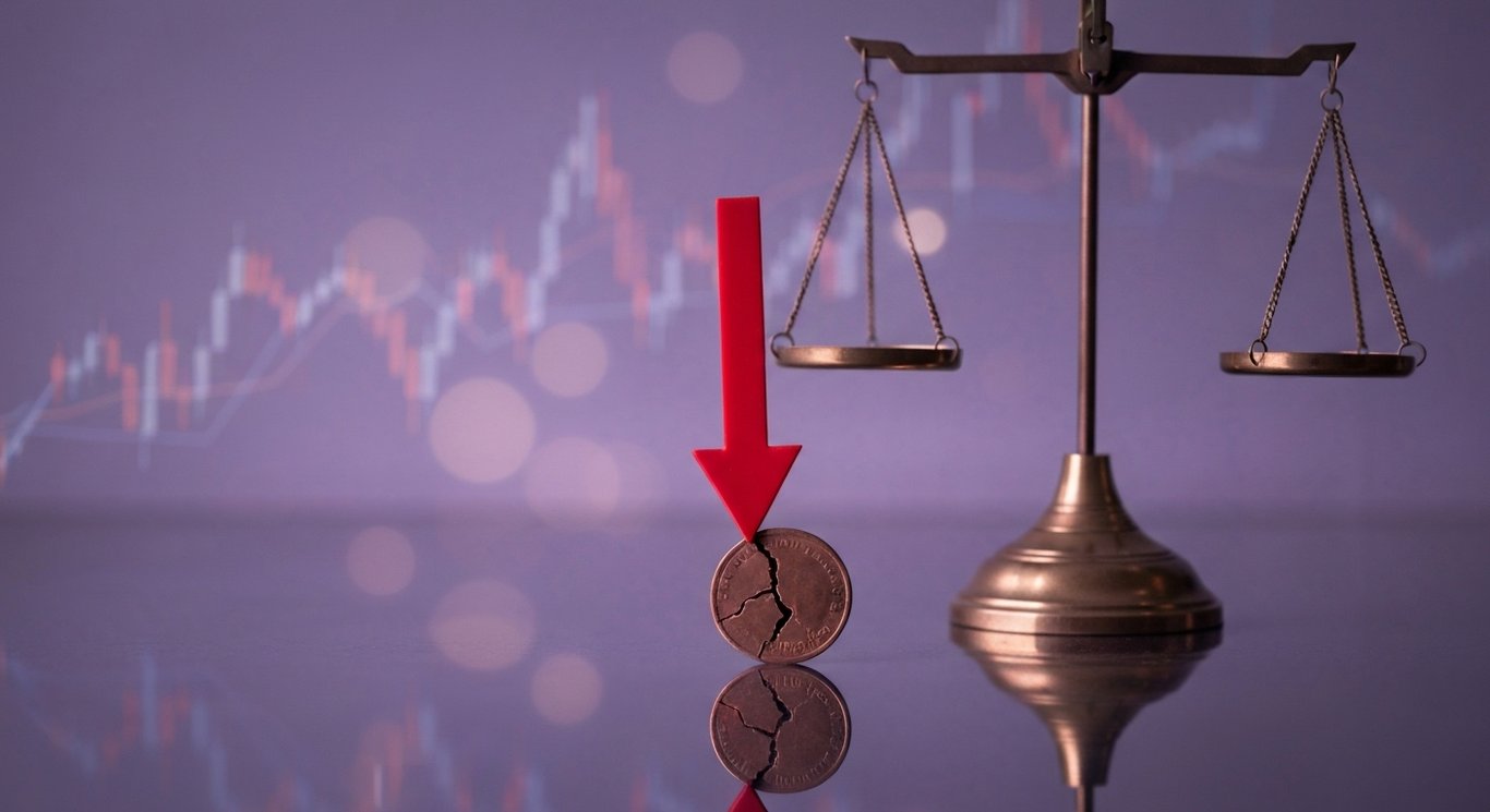 Red downward arrow over cracked coin and balance scale on reflective surface with faint market graph lines