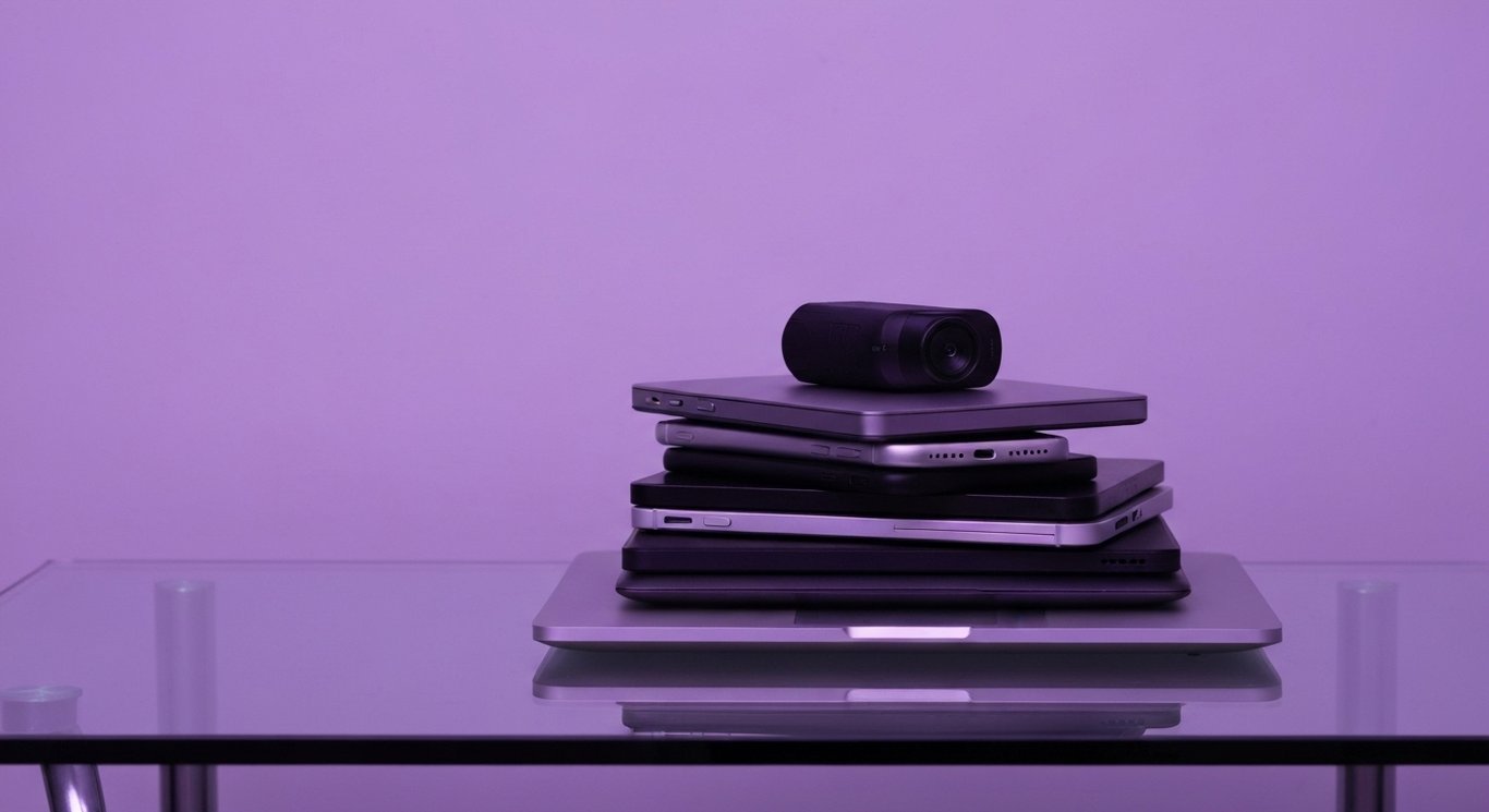 Stack of digital devices on a glass desk with subtle purple lighting