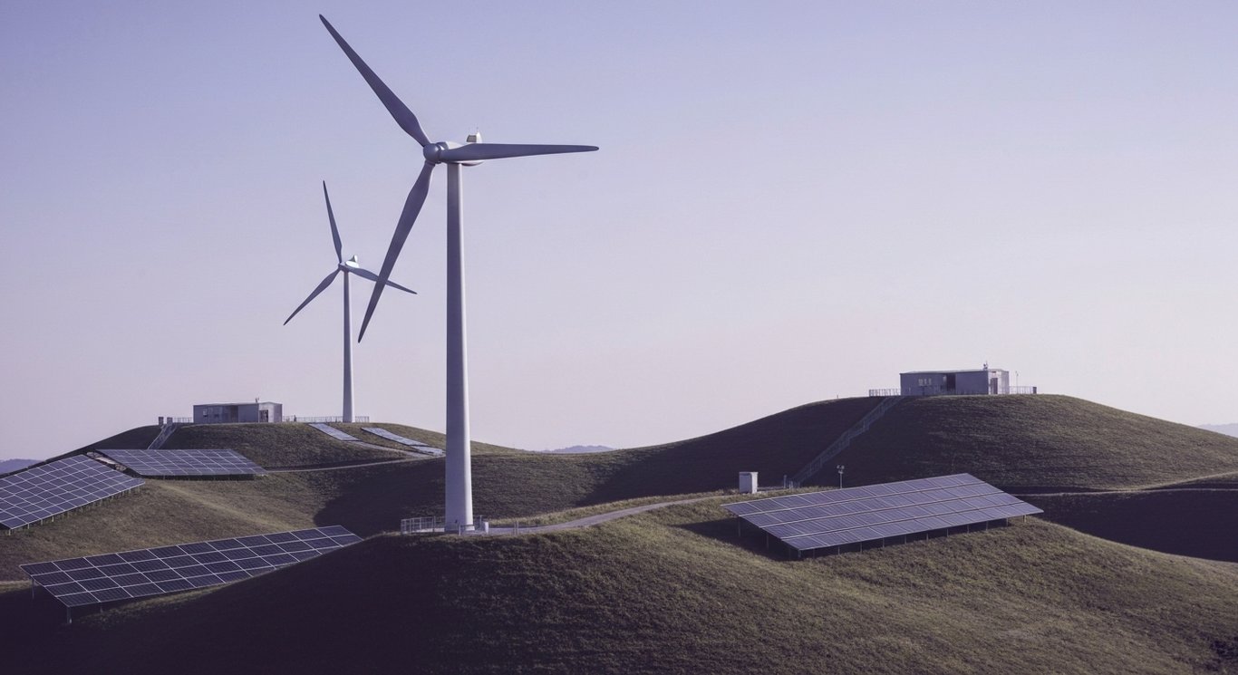 Wind turbines and solar panels on green hills beneath a clear purple-tinted sky