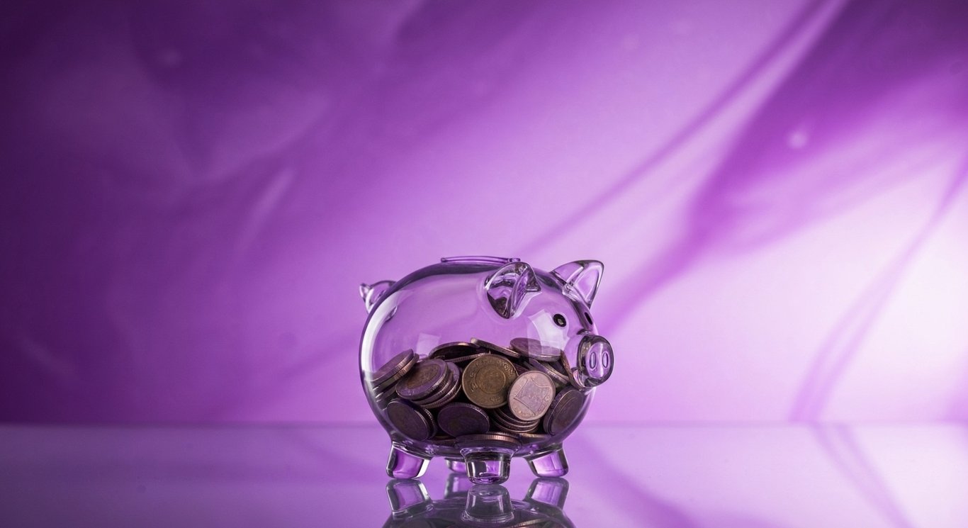Glass piggy bank with coins on a reflective surface and a soft purple gradient background