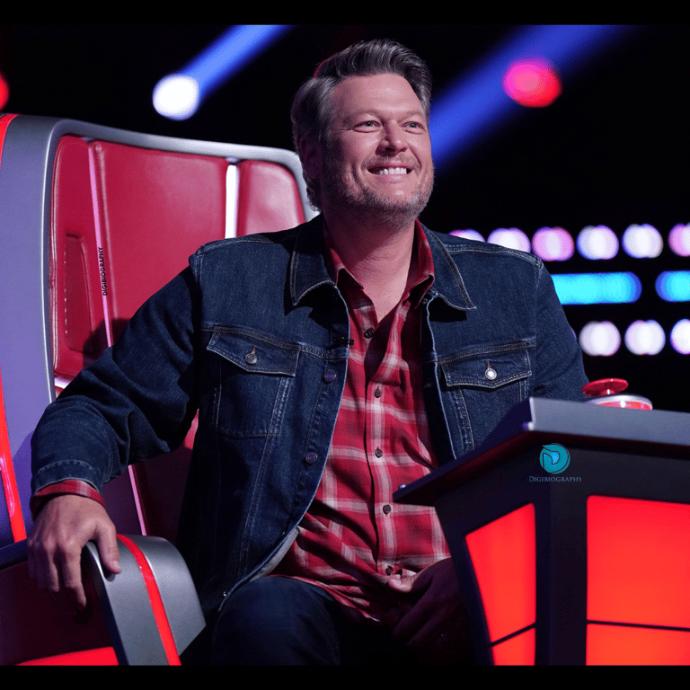 Blake Shelton wearing a blue jacket and sitting on the chair