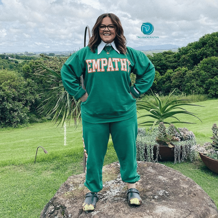 Melissa McCarthy wearing a green dress and stands on the stone