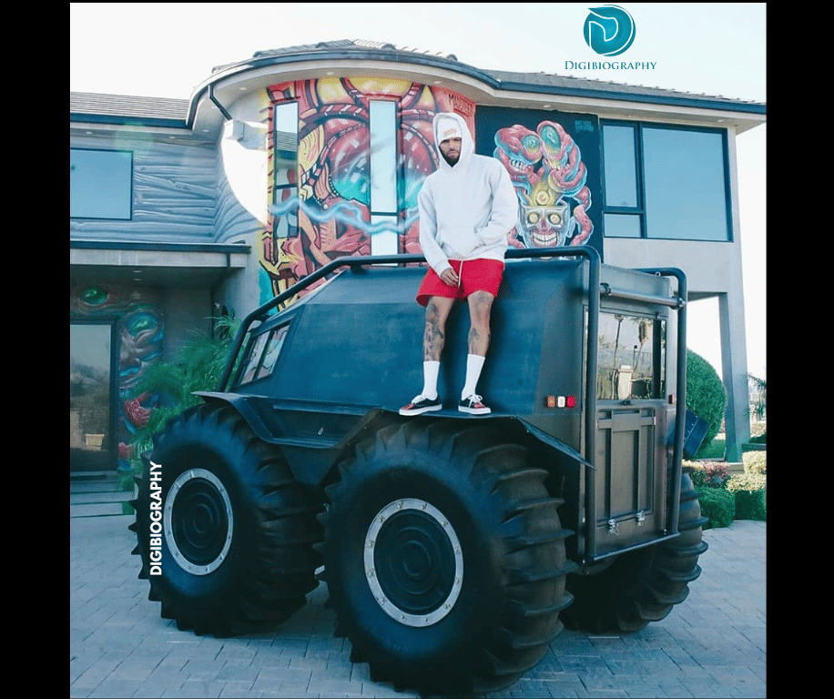 Kanye West wearing a white hoodie and standing on her monster car