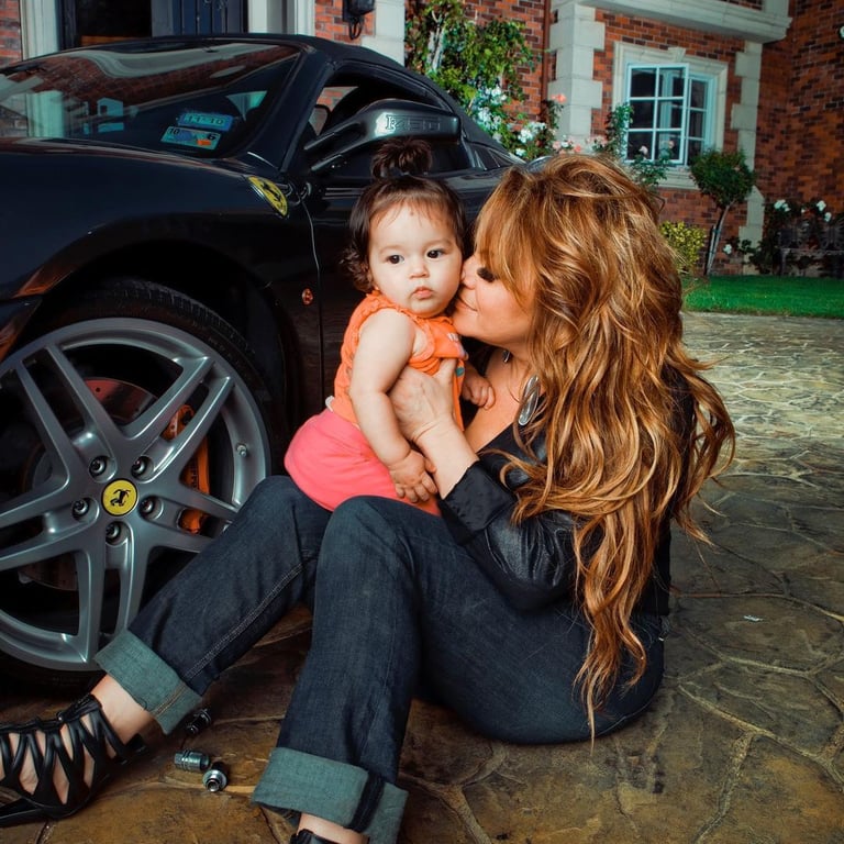 Jenni Rivera sitting nearby the car while giving a kiss to their daughter