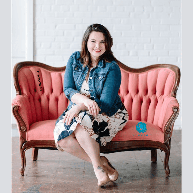 Melissa McCarthy sitting on the sofa while wearing a blue jacket with a white dress