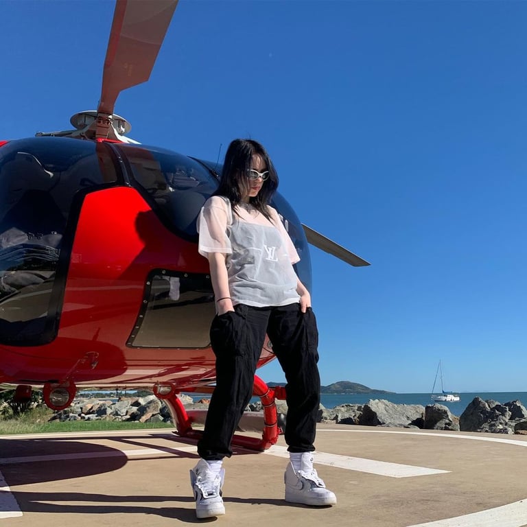 Billie Eilish standing on a helipad in front of the helicopter.