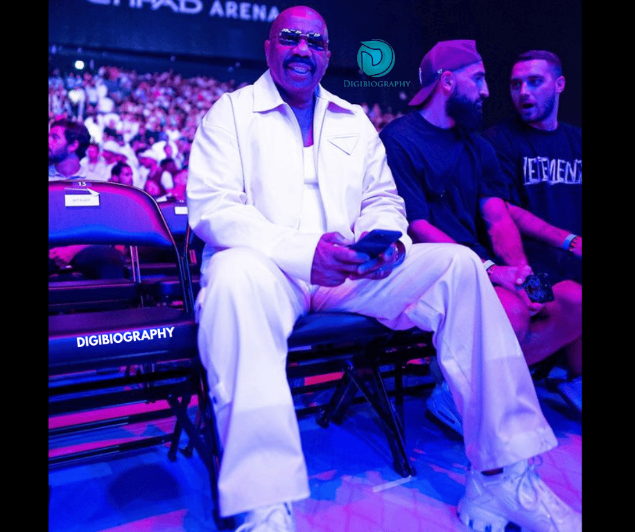 Steve Harvey sitting on a chair and wearing a white shirt