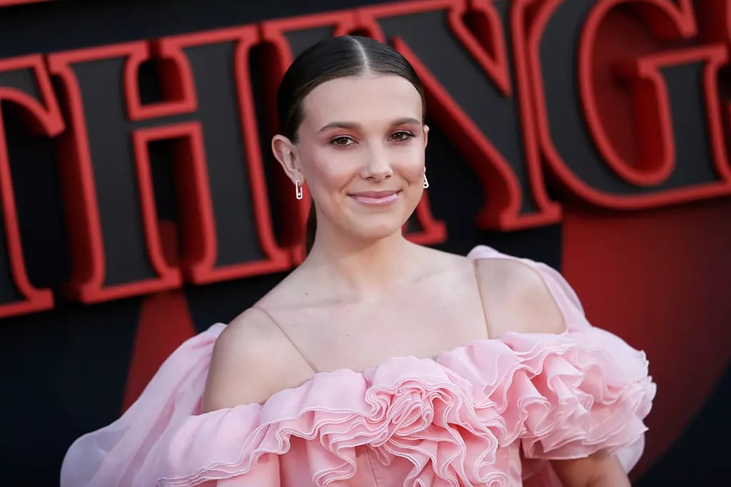 Millie Bobby Brown standing in an award show wearing a pink flower dress