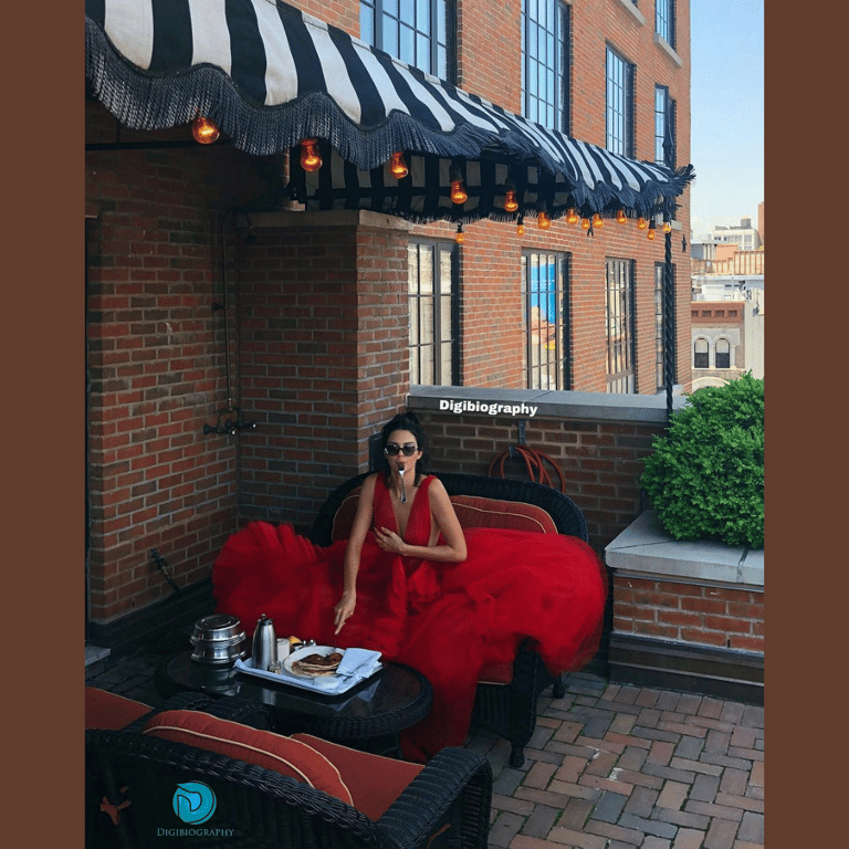 Kendall Jenner wearing a red dress and sitting in the table out side of his house