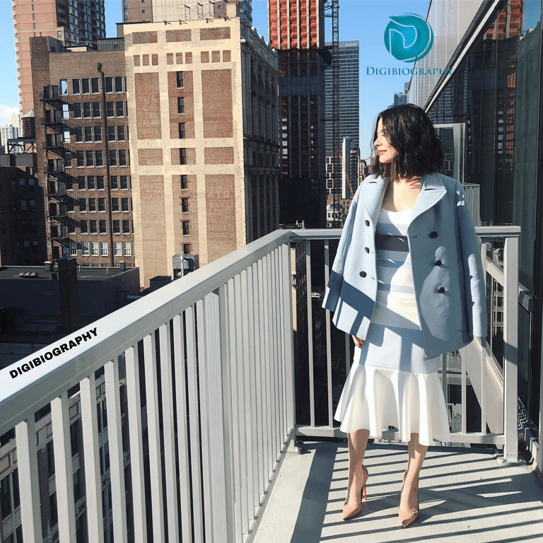 Miranda Cosgrove standing on her balcony and wears a white dress with blazer