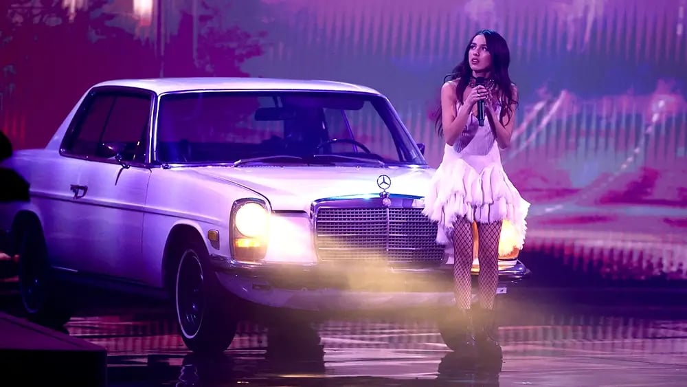 Olivia Rodrigo standing with a Mercedes car and singing a song in concert